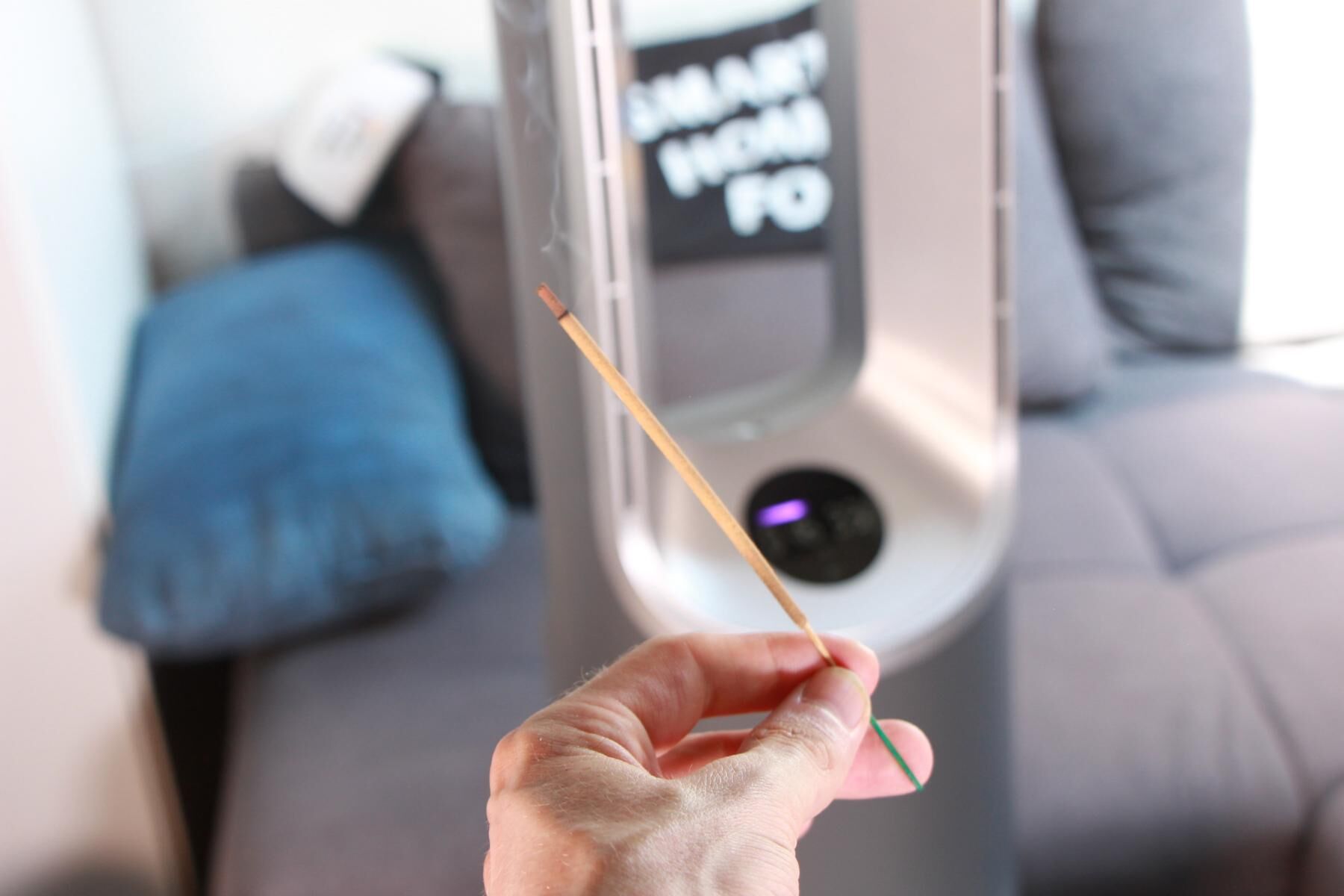 Ein Räucherstäbchen brennt und qualmt und der Philips Air Performer Series 8000 (AMF870/15) steht eingeschaltet im Hintergrund auf einem Couchtisch und das Display zeigt schwache Luftqualität an.